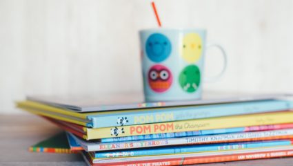 Short stack of colorful children's books and a mug on top of them