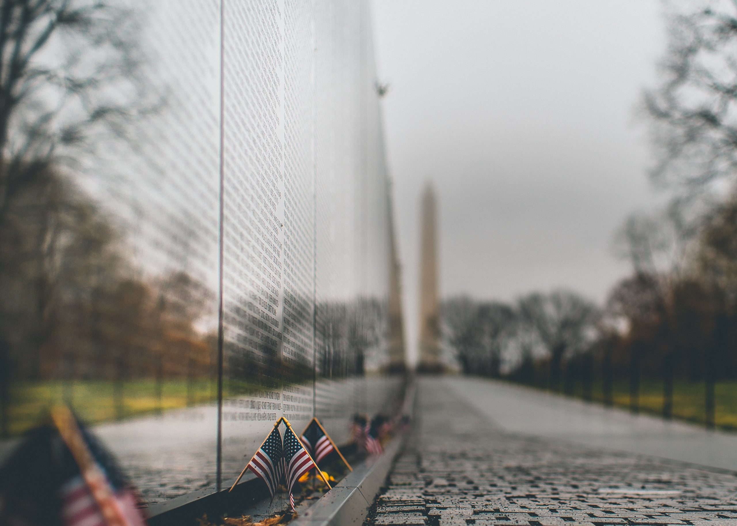 Vietnam Veterans Memorial wall with small American flags and Washington Monument in background
