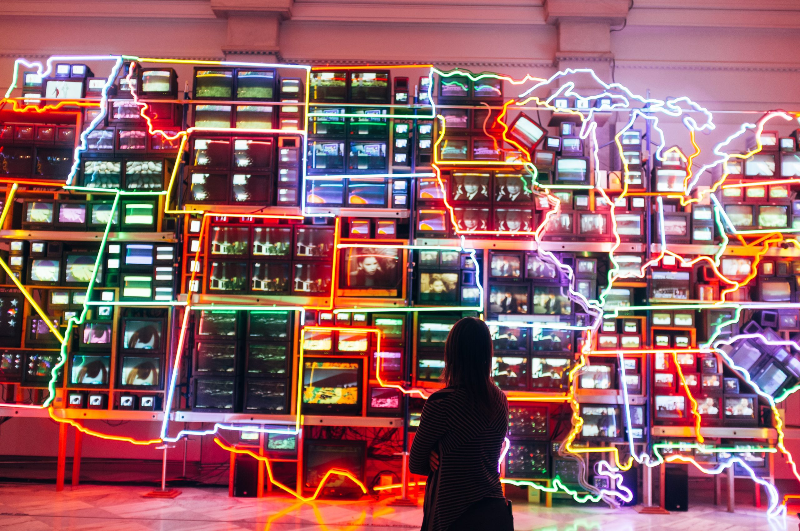 A visitor stands before a vibrant wall of neon screens glowing with color