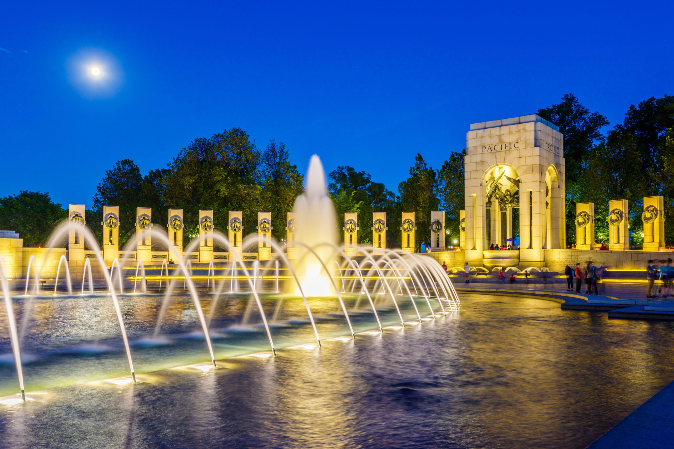 World War II Memorial fountain illuminated at night with Pacific arch in Washington DC