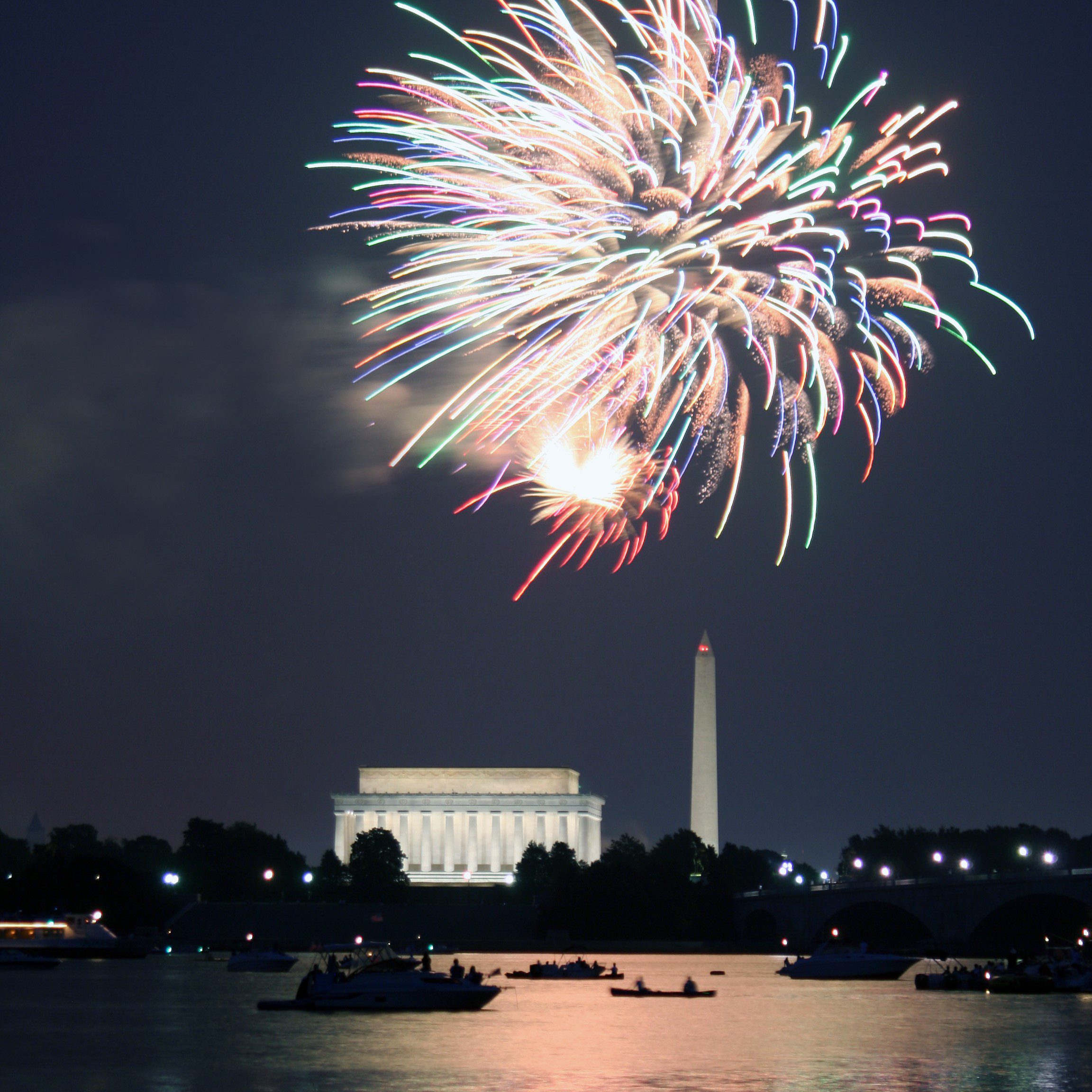 Fireworks illuminating the Lincoln Memorial and Washington Monument over the Potomac at night.